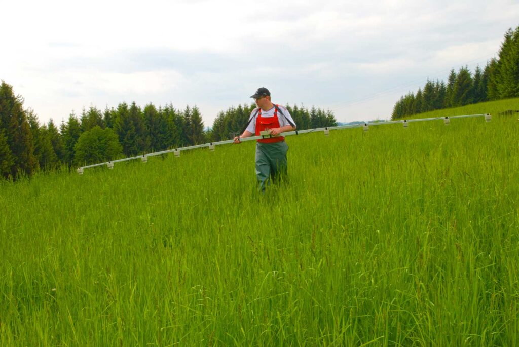 Ein Mann sucht mit dem System "Infrarot Wildretter" von ISA Industrieelektronik, einer fünf Meter lange Stange mit Infrarotsensoren, ein Feld nach Rehkitzen ab
