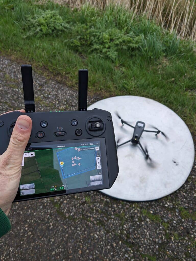 Fernsteuerung mit Drohne auf Landepad im Hintergrund. Die Fernsteuerung zeigt PinPoints die zuvor markiert wurden.