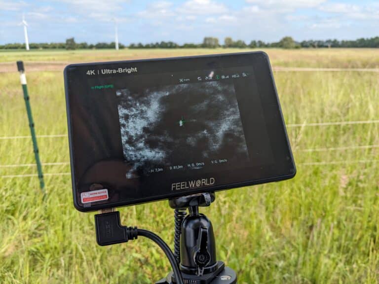 Bildschirm vor einer Wiese. Auf dem Bildschirm ist das Wärmebild eines Rehkitzes zu sehen.